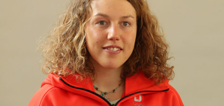 Porträt der deutschen Biathletin Laura Dahlmeier in roter Sportjacke mit lockigen, hellbraunen Haaren und türkisfarbenem Halsschmuck. Quelle: Martin Rulsch, Wikimedia Commons, CC BY-SA 4.0.