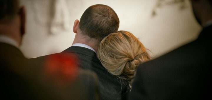 Trauernde Angehörige bei einer Beerdigung – eine Frau sucht Trost, indem sie ihren Kopf an die Schulter eines Mannes lehnt.