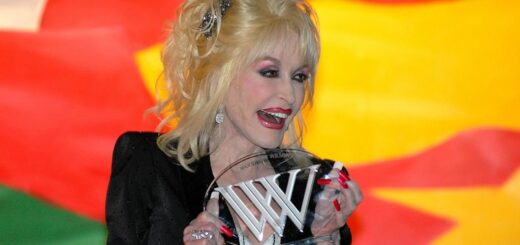 Dolly Parton bei einer Preisverleihung, lächelnd mit einer gläsernen Trophäe in den Händen vor einem farbenfrohen Hintergrund.