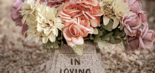 Grabstein mit der Aufschrift „In Loving Memory“, geschmückt mit einem Strauß aus rosa, orangefarbenen und weißen Blumen.